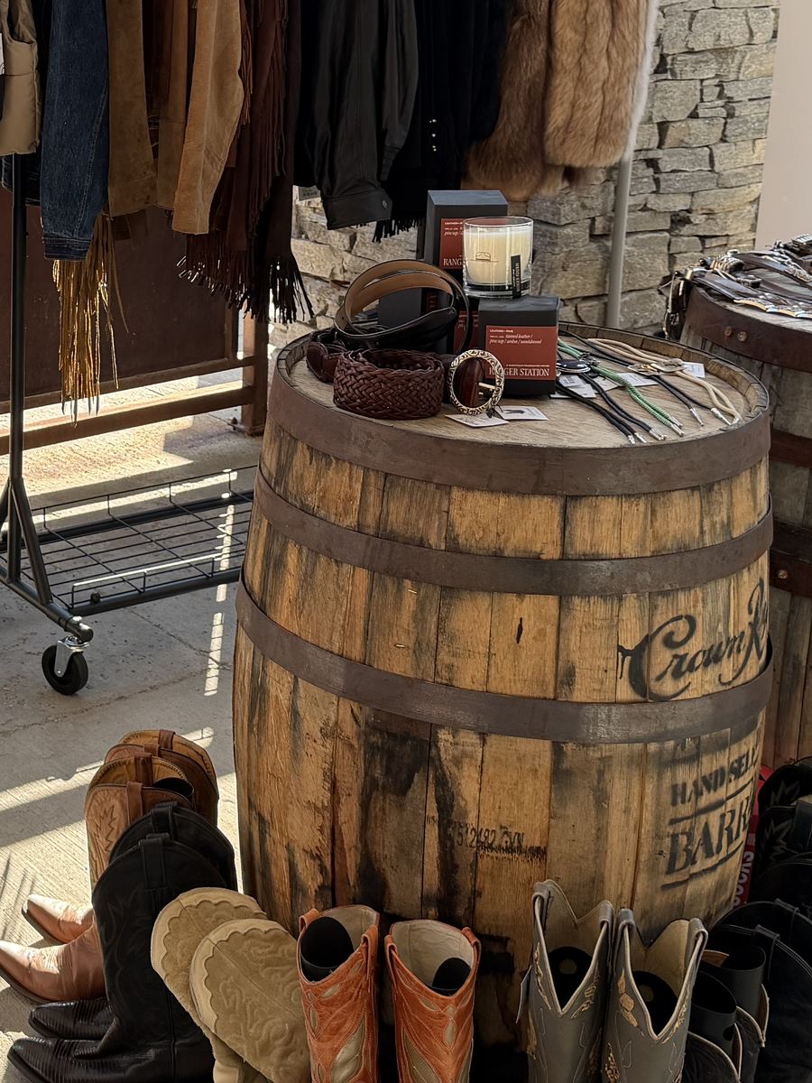Belts and a candle on a whiskey barrel, western boots lined up at its base
